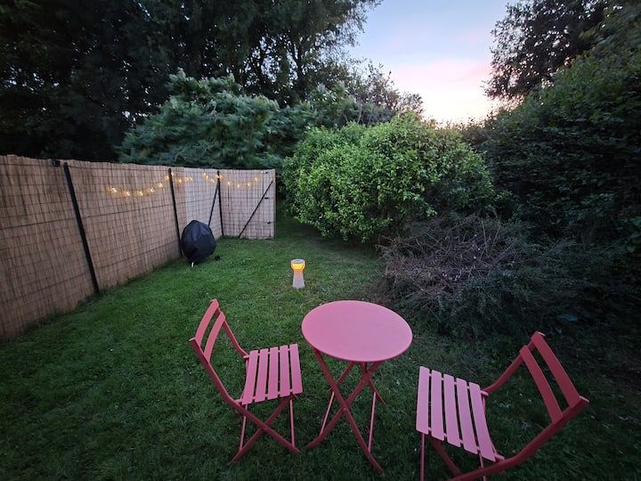 Table et chaises de patio rouges dans un jardin gazonné au crépuscule, avec une petite lumière près de la clôture.