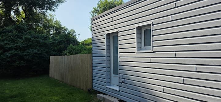 Maison à façade blanche avec porte, fenêtre et clôture en bois, donnant sur une pelouse verte.