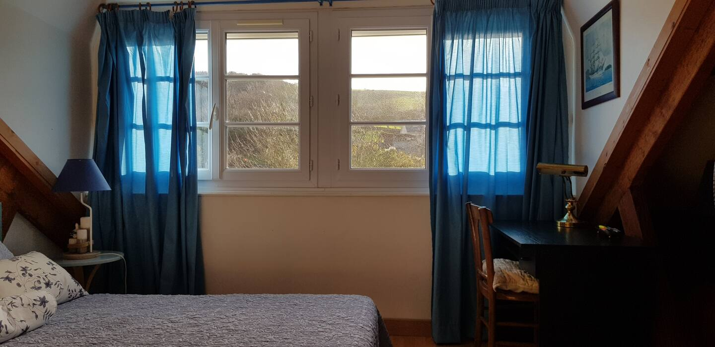 Une chambre avec un lit, un bureau, une chaise et des rideaux bleus.