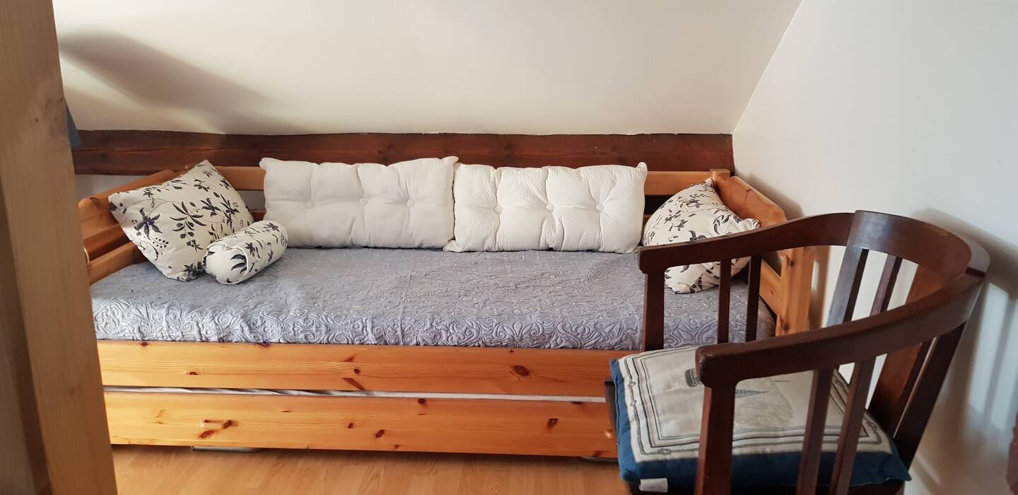 Un canapé en bois avec des coussins blancs et une chaise dans une pièce.