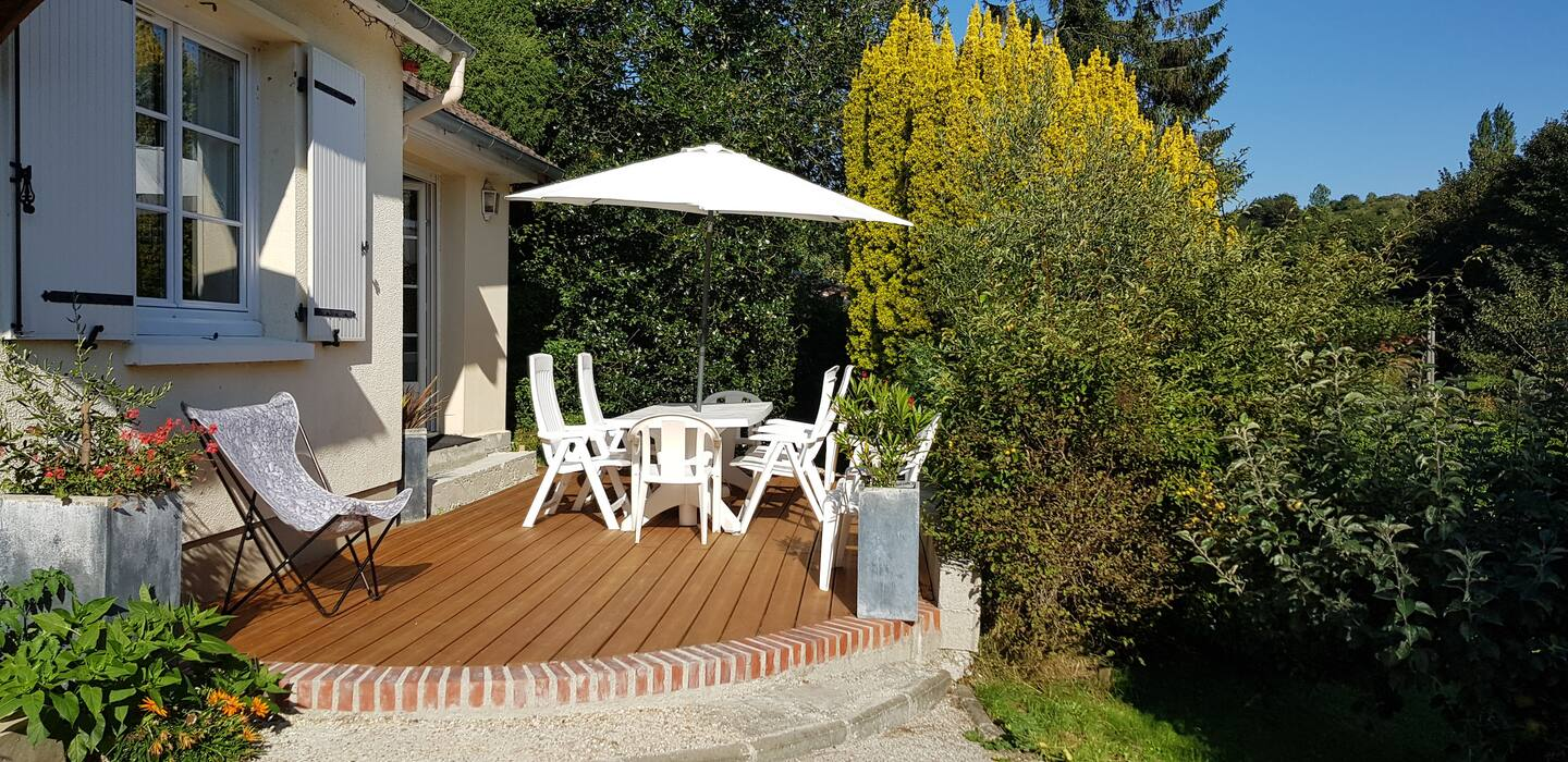 Une terrasse en bois avec une table et des chaises sous un parasol devant une maison.