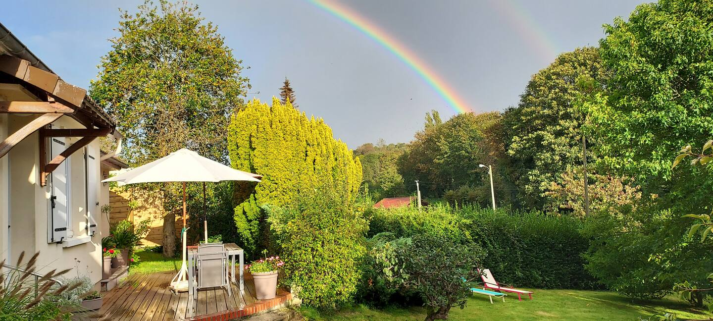 Un arc-en-ciel est visible au-dessus d'un jardin avec une maison en arrière-plan.