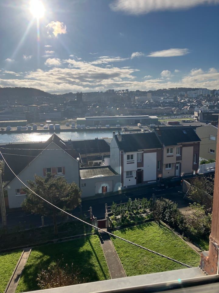 Vue ensoleillée sur des maisons, un jardin verdoyant et des collines au-delà d'une ville côtière