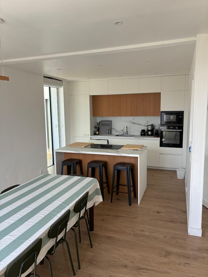 Cuisine et salle à manger modernes avec placards blancs, touches de bois, tabourets de bar et nappe à rayures