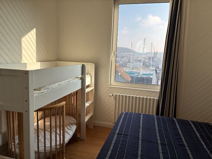 Petite chambre avec lit superposé, couvre-lit rayé et fenêtre donnant sur un port.