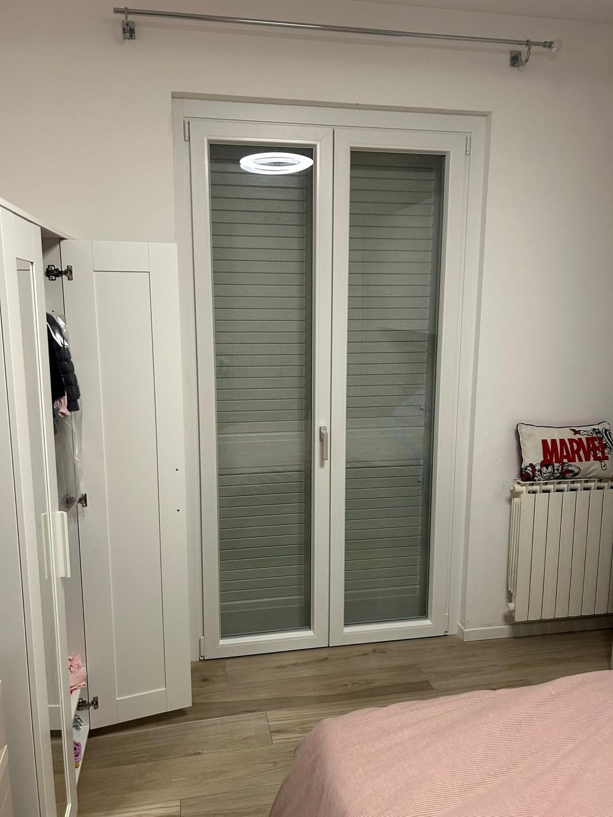 Porte doppie bianche con persiane chiuse, un armadio e un termosifone in una camera da letto.