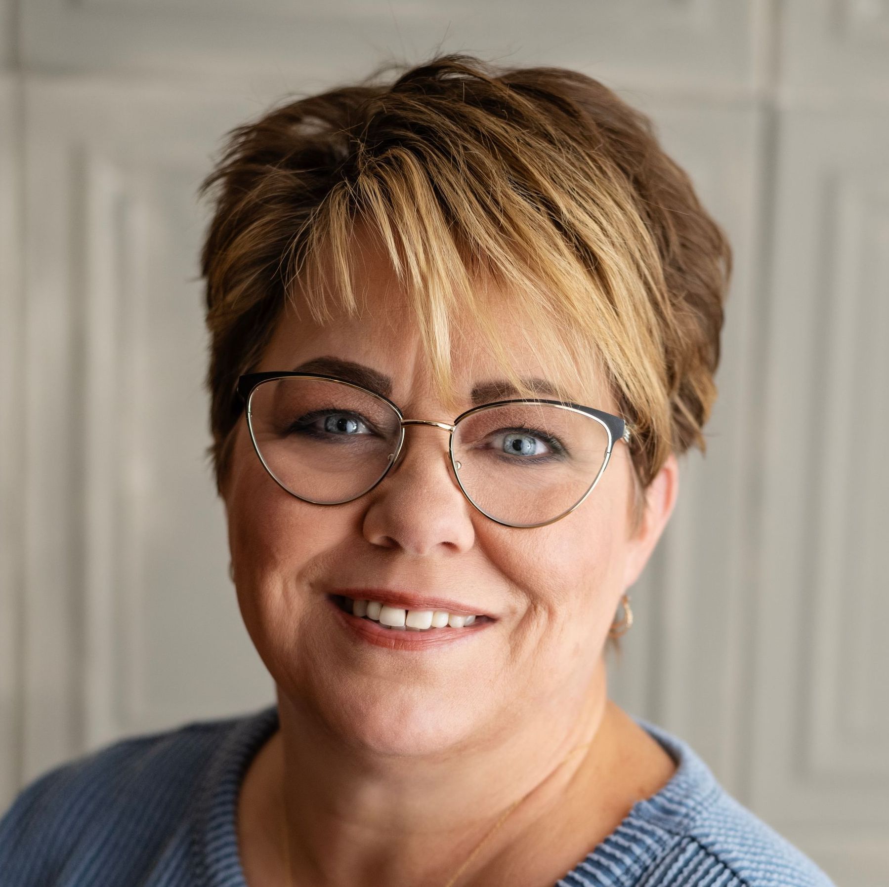 Woman with short brown and blonde hair wearing glasses smiles at the camera.