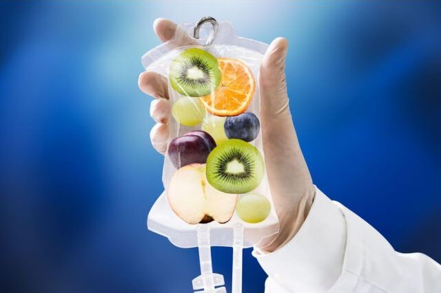 Hand holding IV bag filled with fruit slices. Blue background.