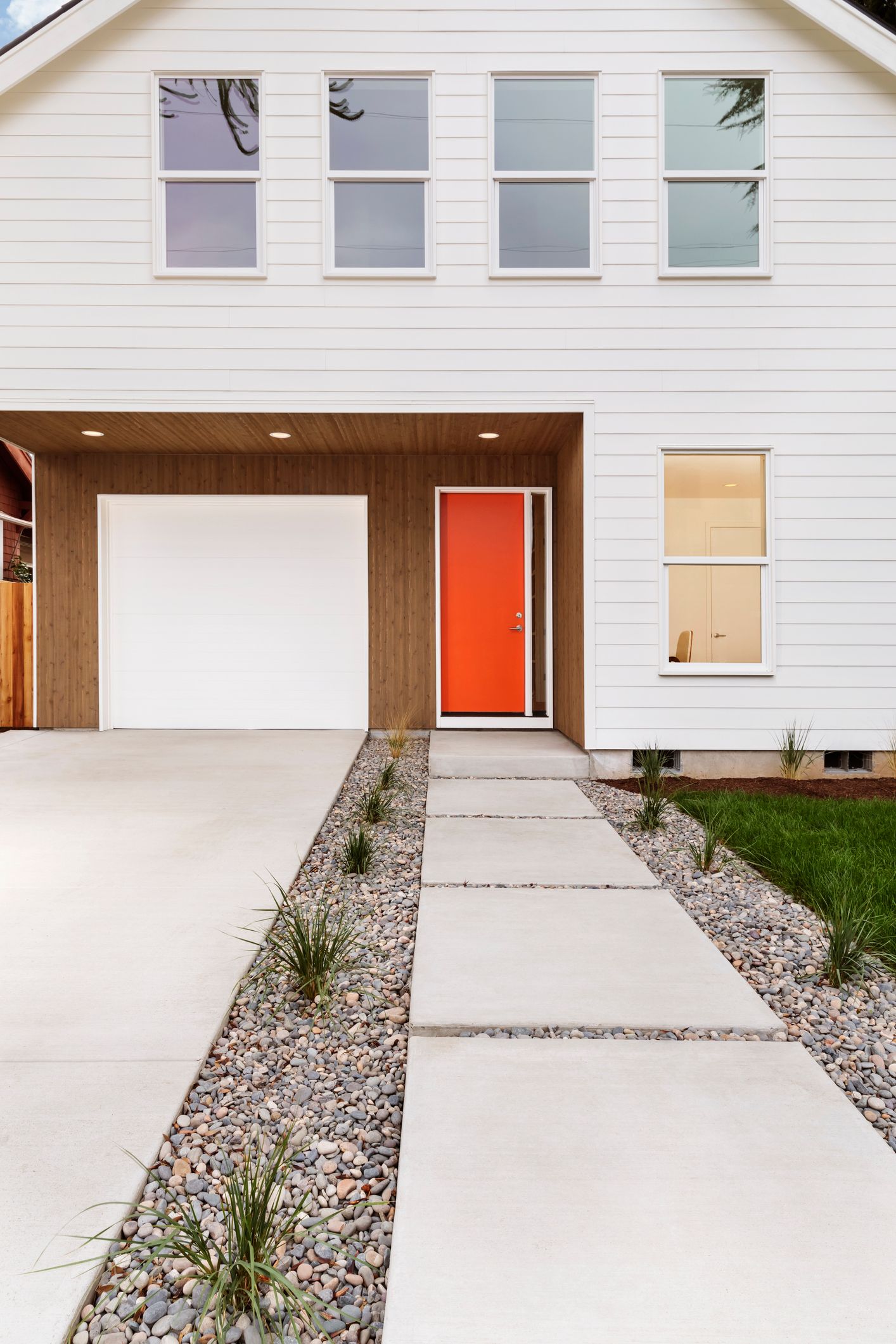 White house with orange door, garage, and a concrete pathway with rock gardens. White house with orange door, garage, and a concrete pathway with rock gardens.