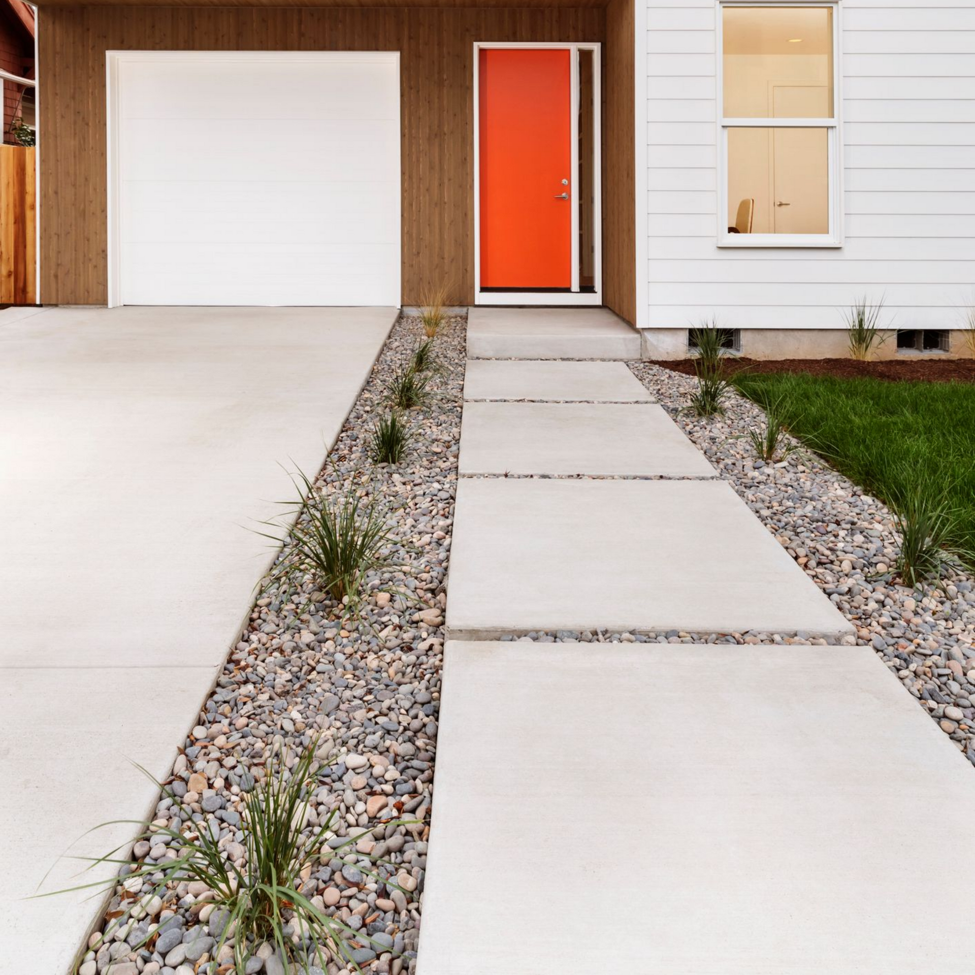 White house with orange door, garage, and a concrete pathway with rock gardens. White house with orange door, garage, and a concrete pathway with rock gardens.