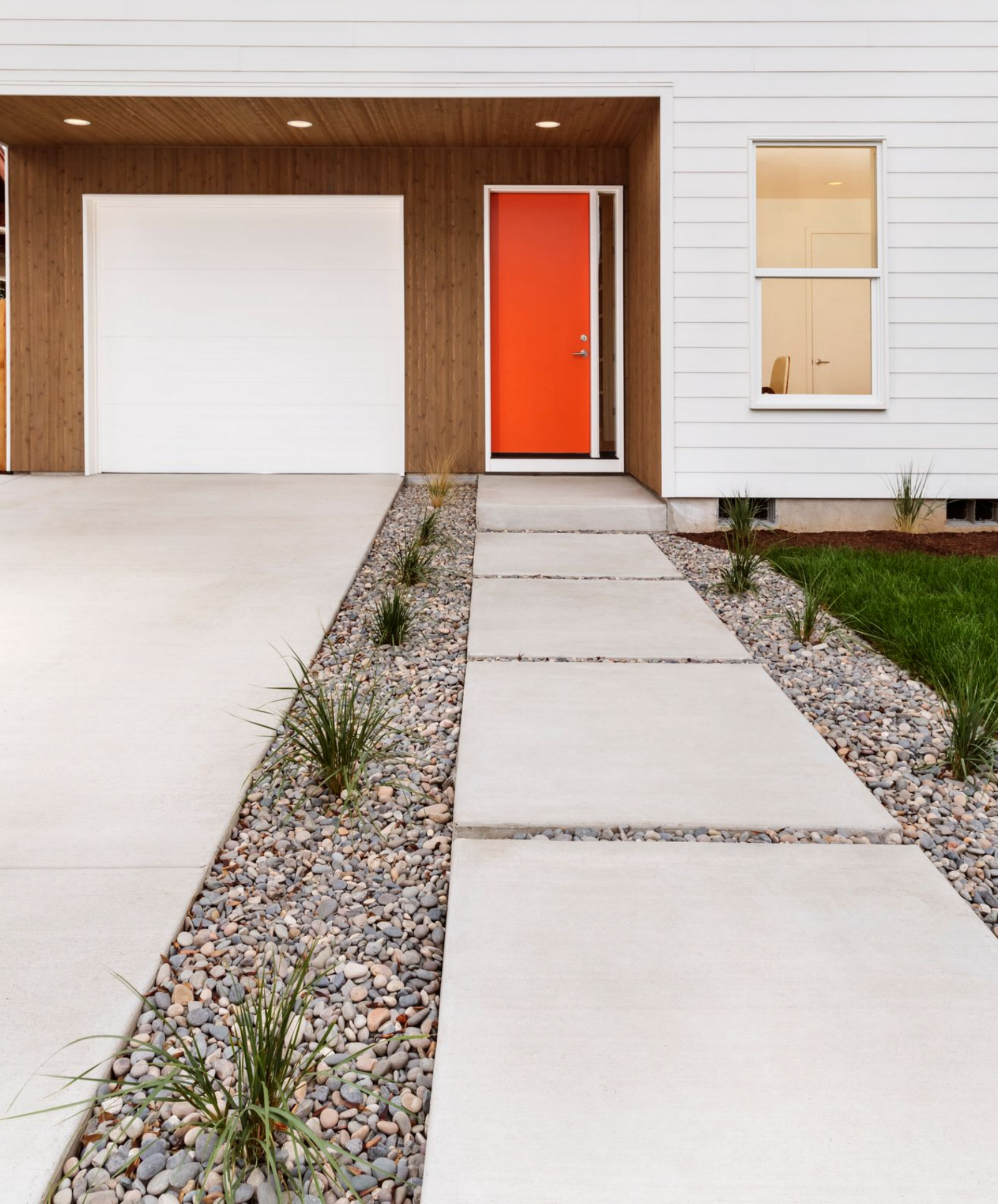 White house with orange door, garage, and a concrete pathway with rock gardens. White house with orange door, garage, and a concrete pathway with rock gardens.