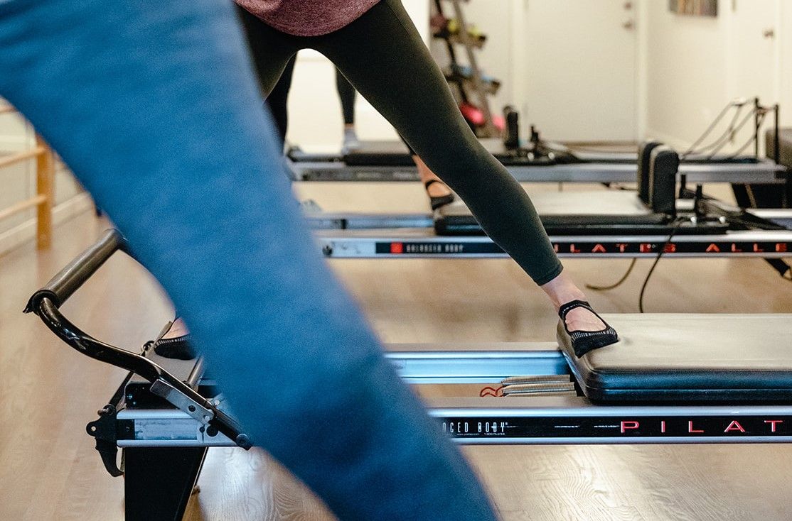 A woman is using a pilates refomer in a gym.