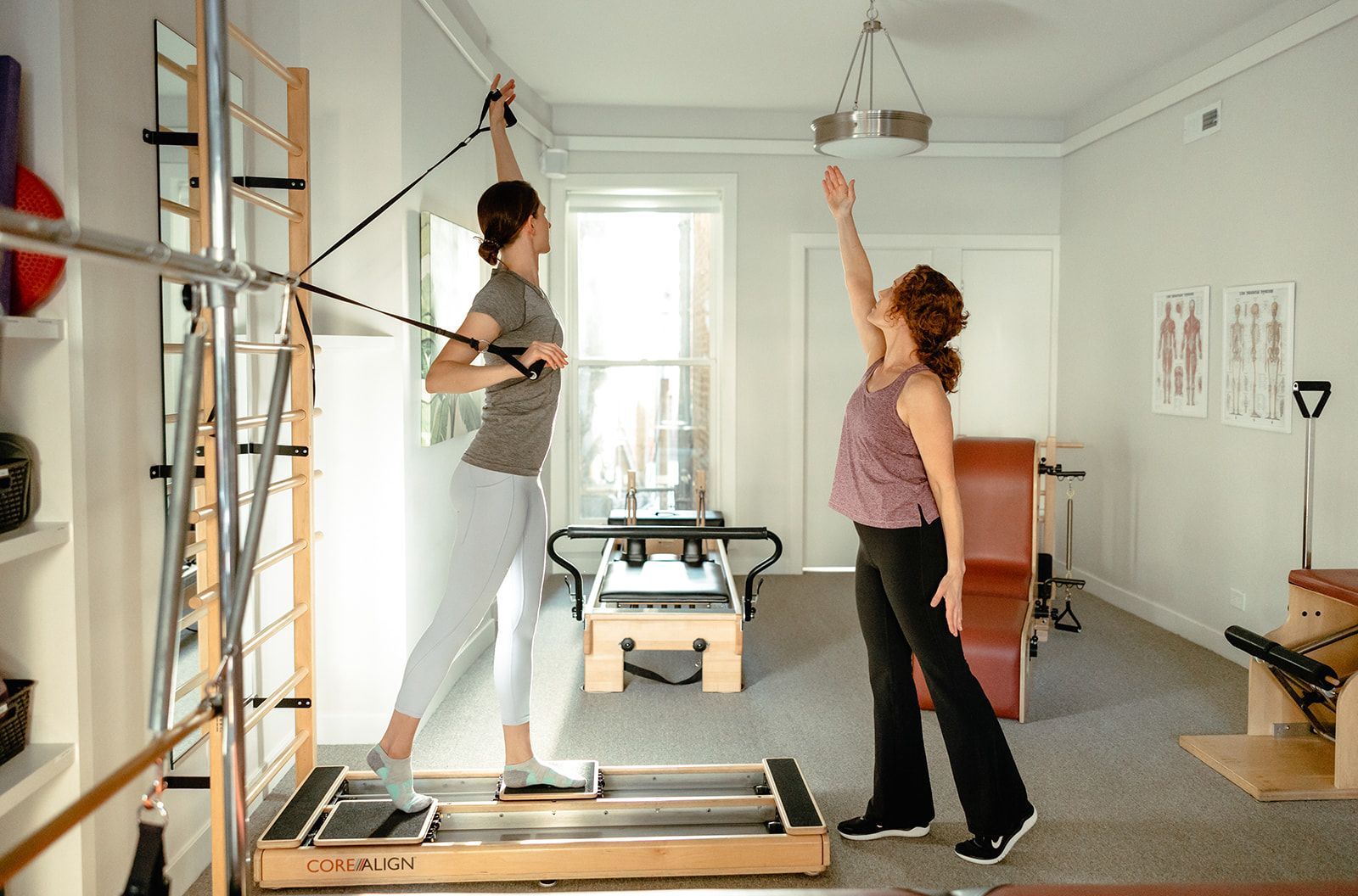 Two women are doing exercises in a pilates studio.