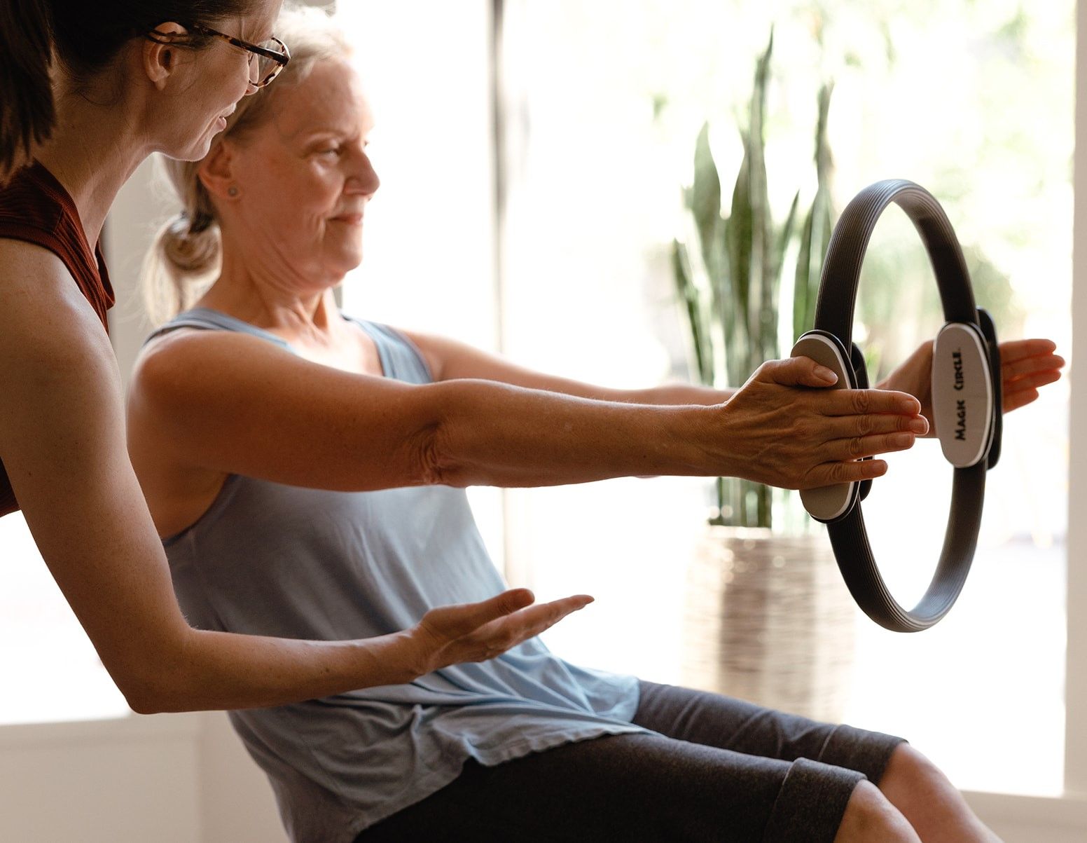 A woman is using a pilates ring while another woman watches.
