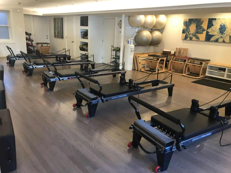 A row of pilates machines are lined up in a studio.