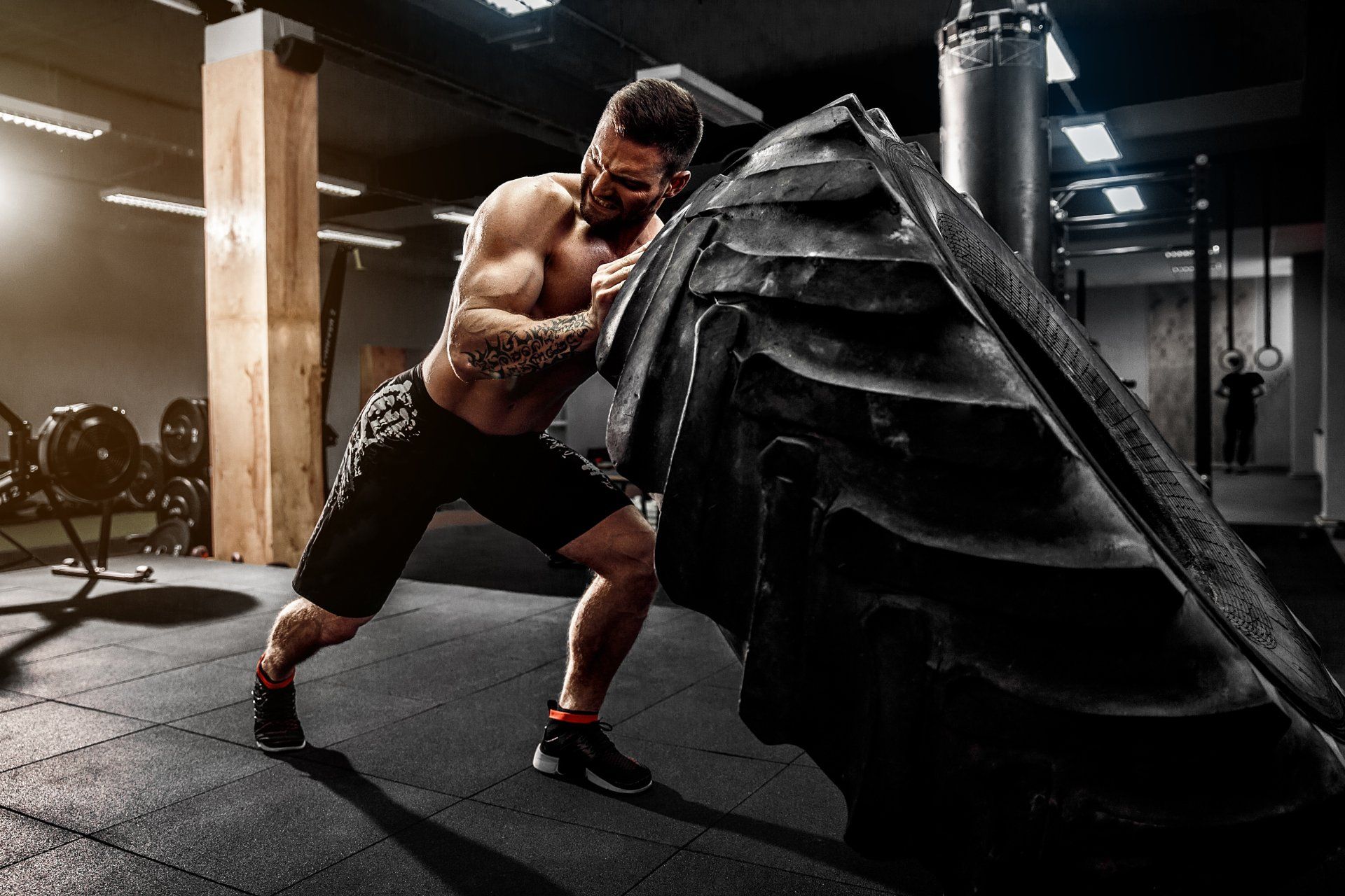 Shirtless man flipping heavy tire at gym.