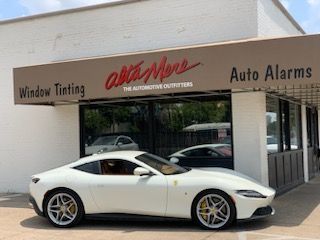 A white sports car is parked in front of a window tinting and auto alarms store.