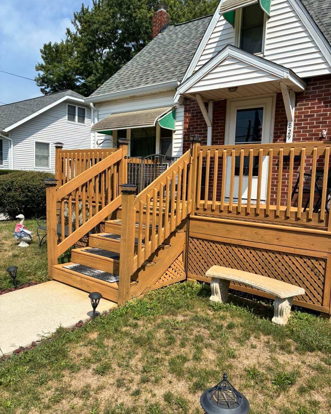 Front porch with wooden stairs and railing on a brick house, beside a sidewalk and lawn