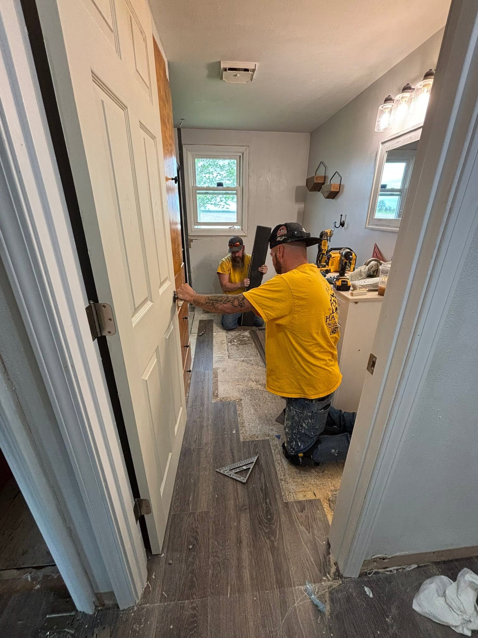 Worker kneeling in a hallway, fixing floorboards during home renovation.