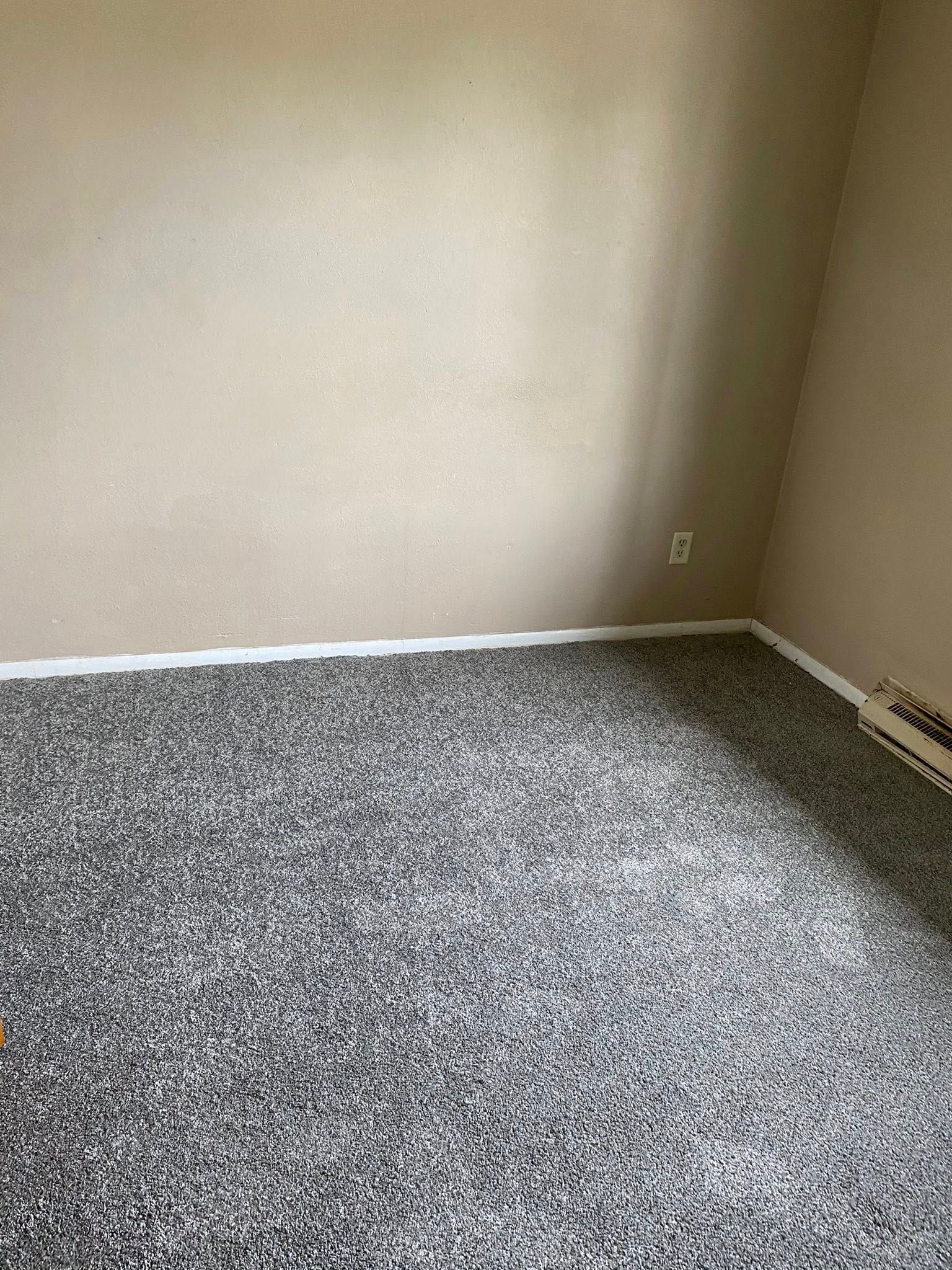 Empty carpeted room with beige walls and white baseboards.