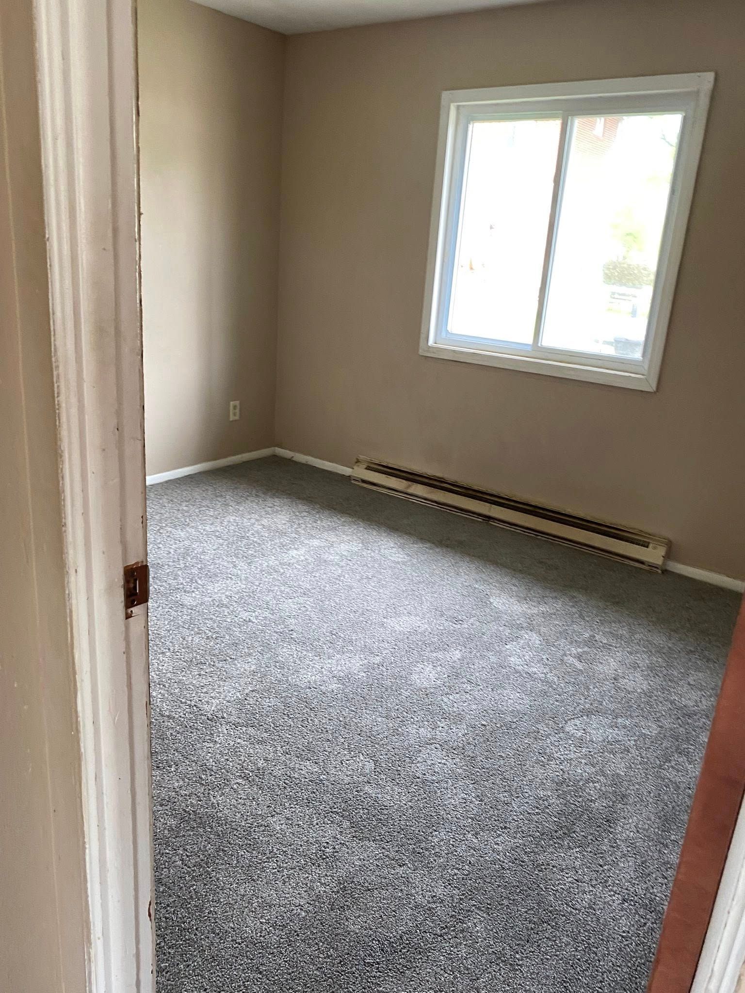 Empty beige bedroom with gray carpet and a window, viewed from the doorway