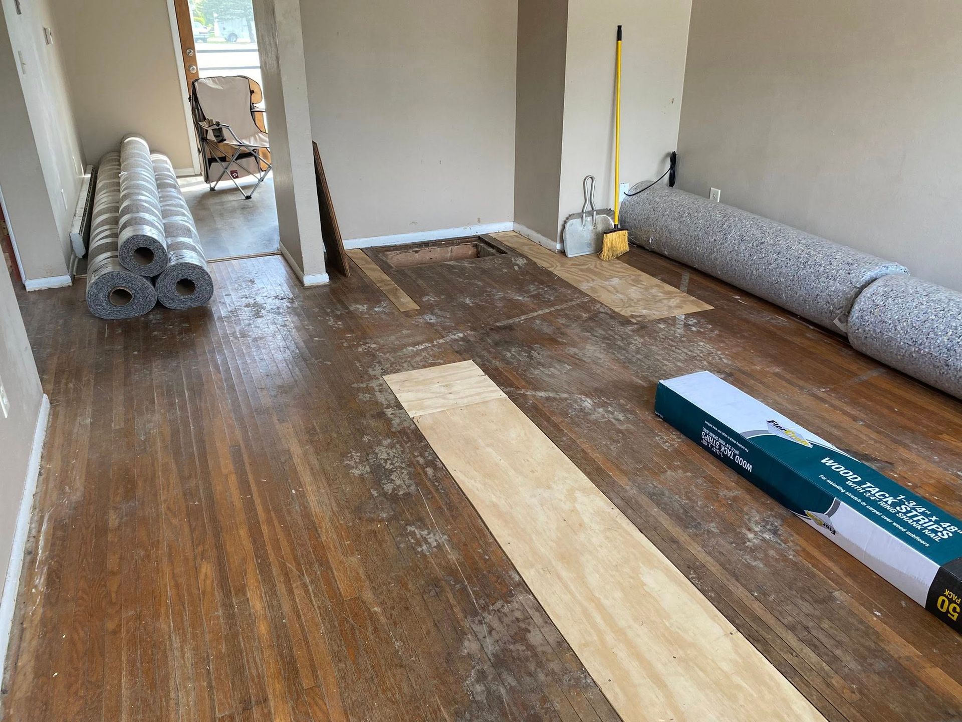 Unfinished room with rolled flooring, tools, and a long strip of wood flooring laid on the floor.
