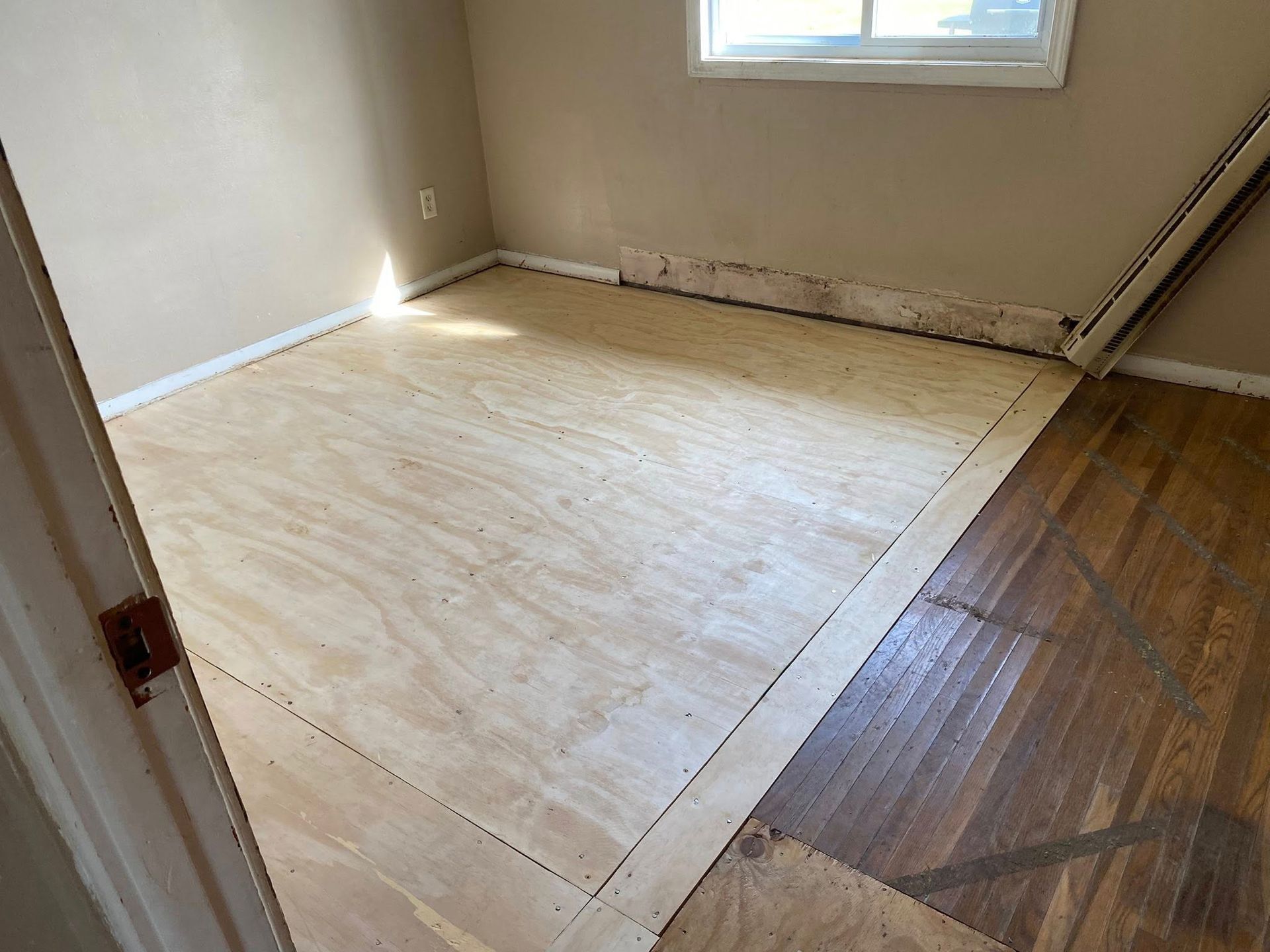 Empty room with bare plywood floor and a window letting in light