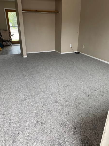 Empty carpeted room with beige walls and a doorway to a hallway or outside area
