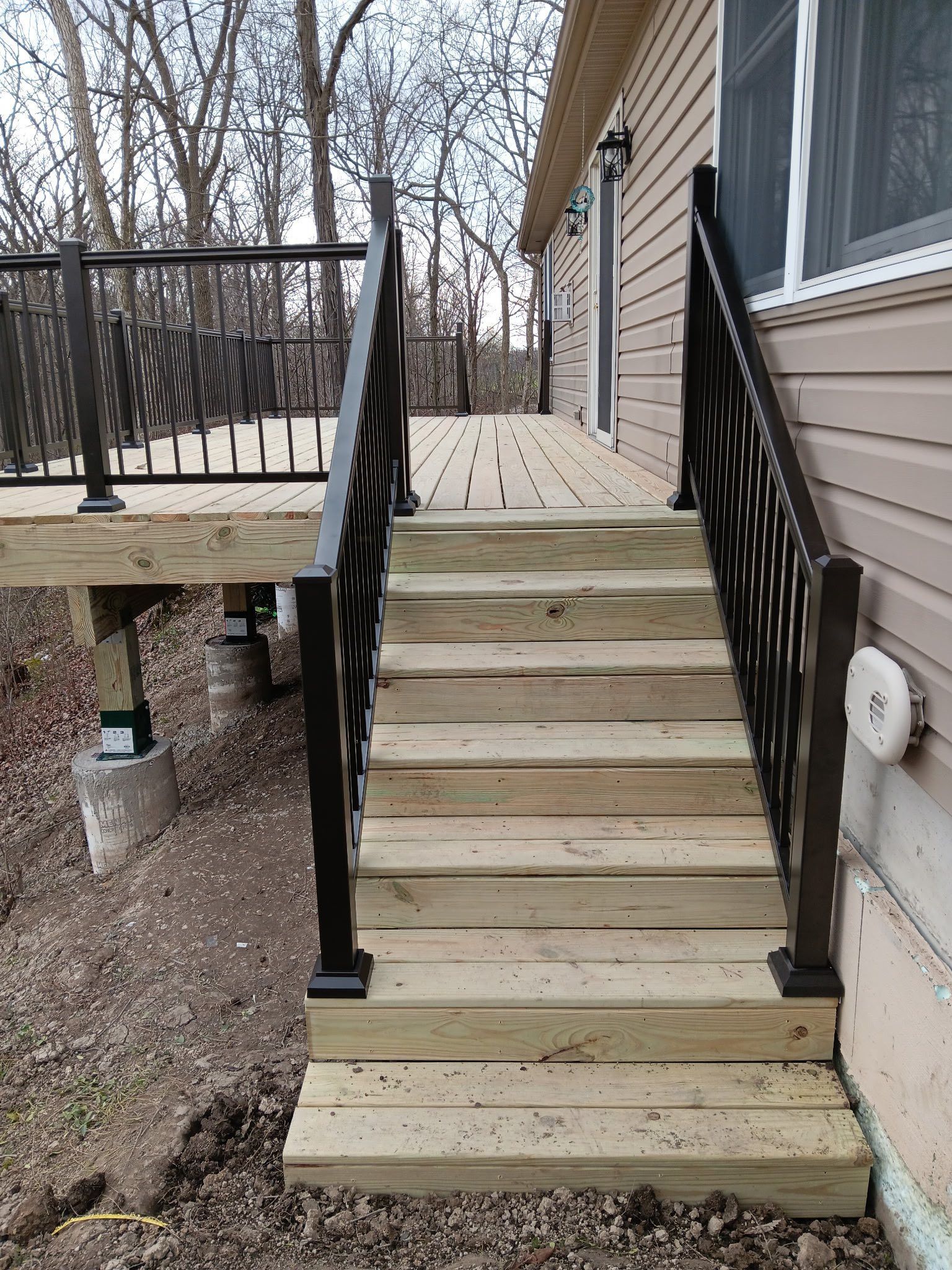 Outdoor wooden staircase with black railings leading up to a beige house deck.
