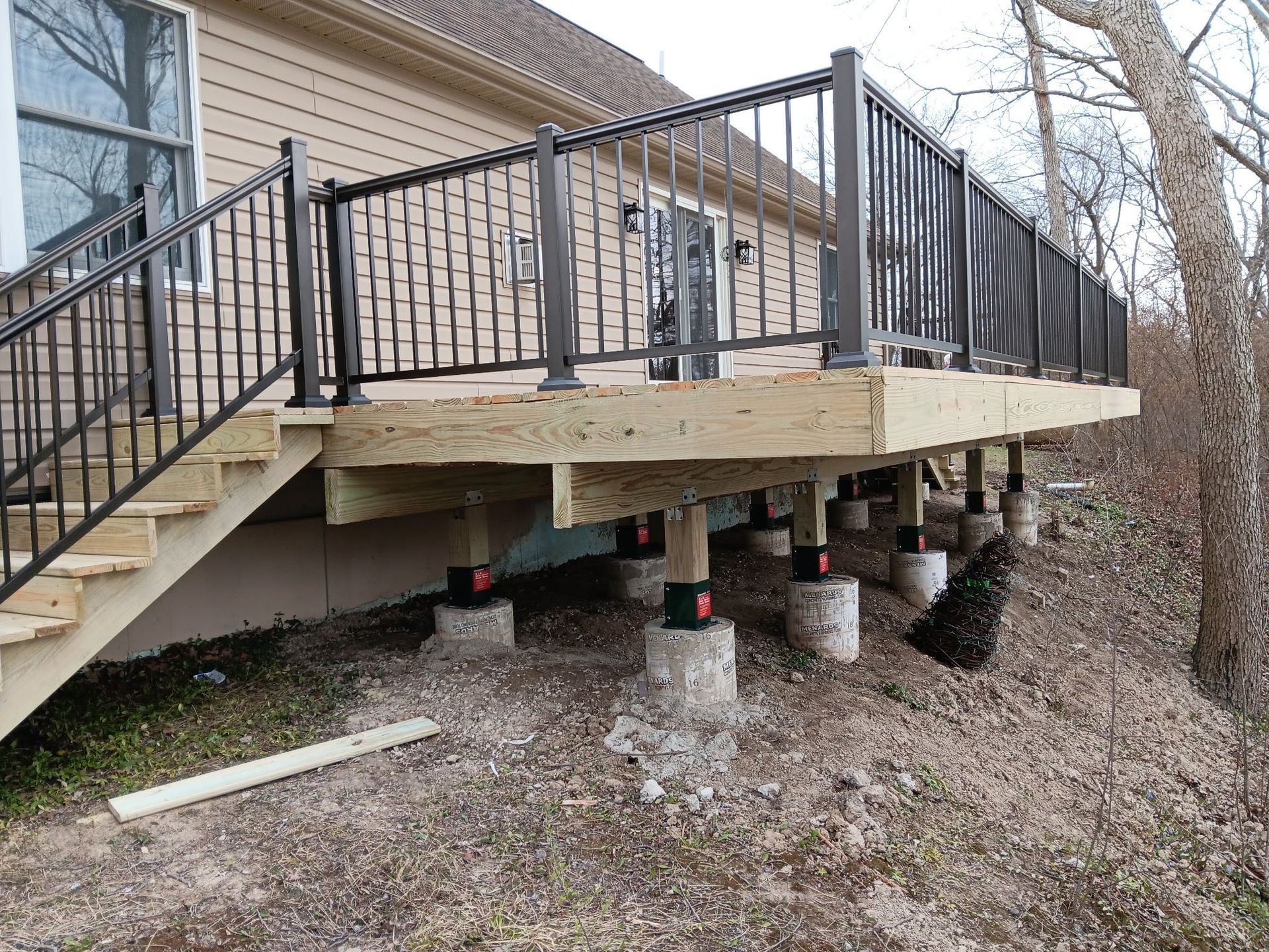 Raised wooden deck with black railing supported by multiple concrete piers beneath a house