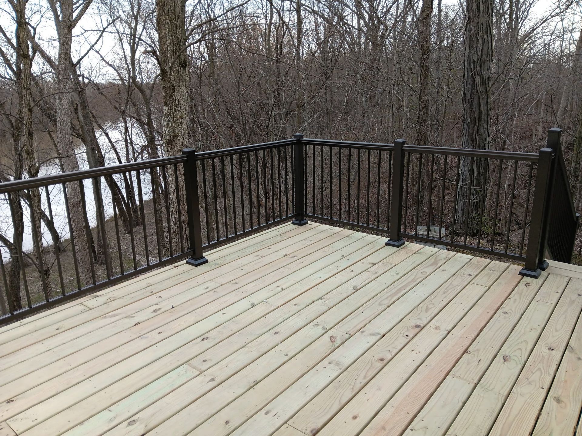 Wooden deck with dark railing overlooking a snowy wooded area