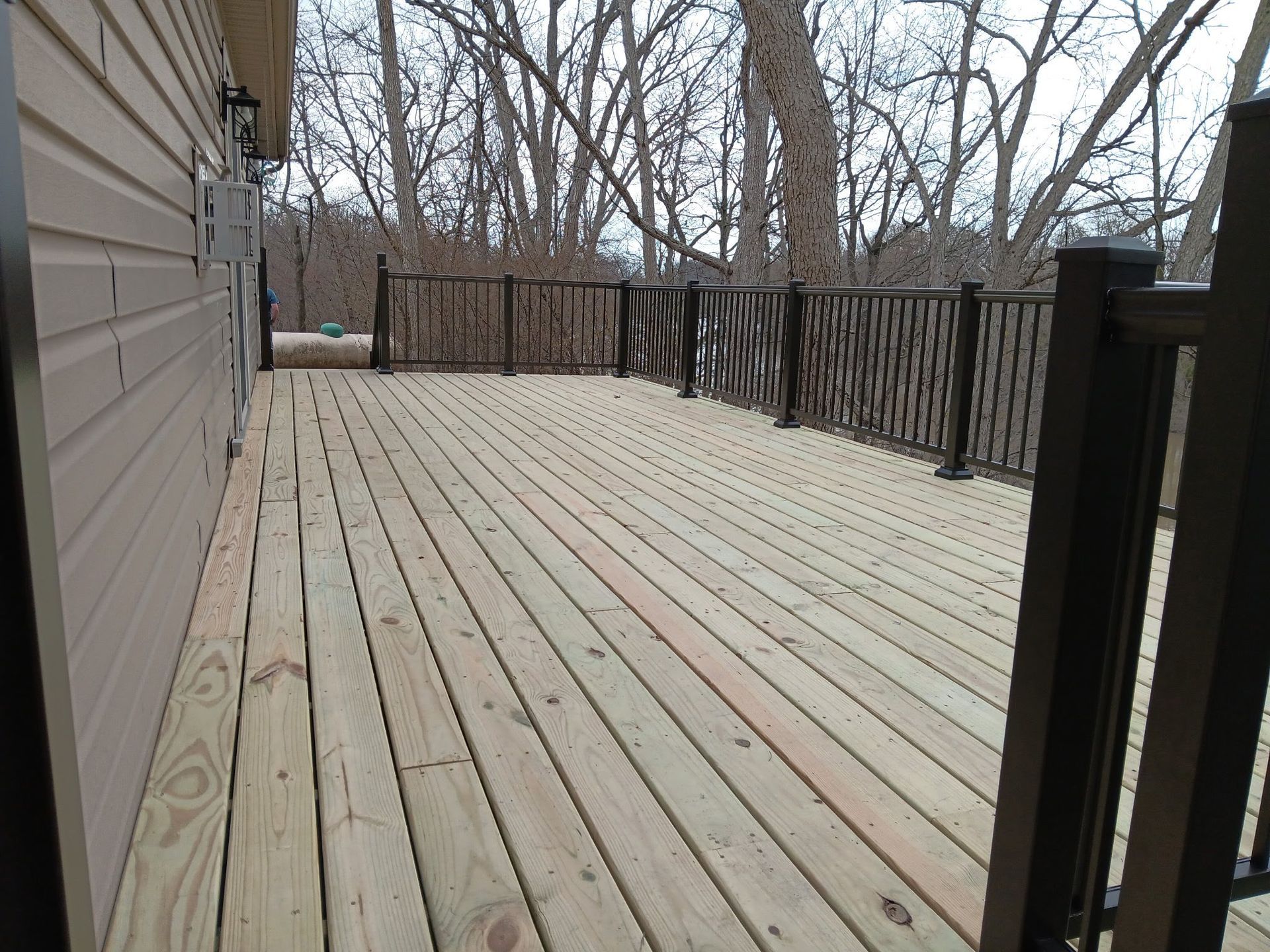 Empty wooden deck with railing, beside a house, in a leafless backyard