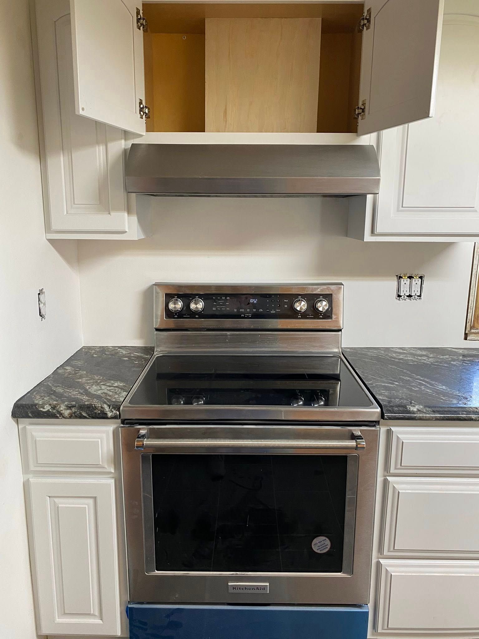 Kitchen with stainless steel stove and hood beneath open upper cabinets, centered between white lower cabinets