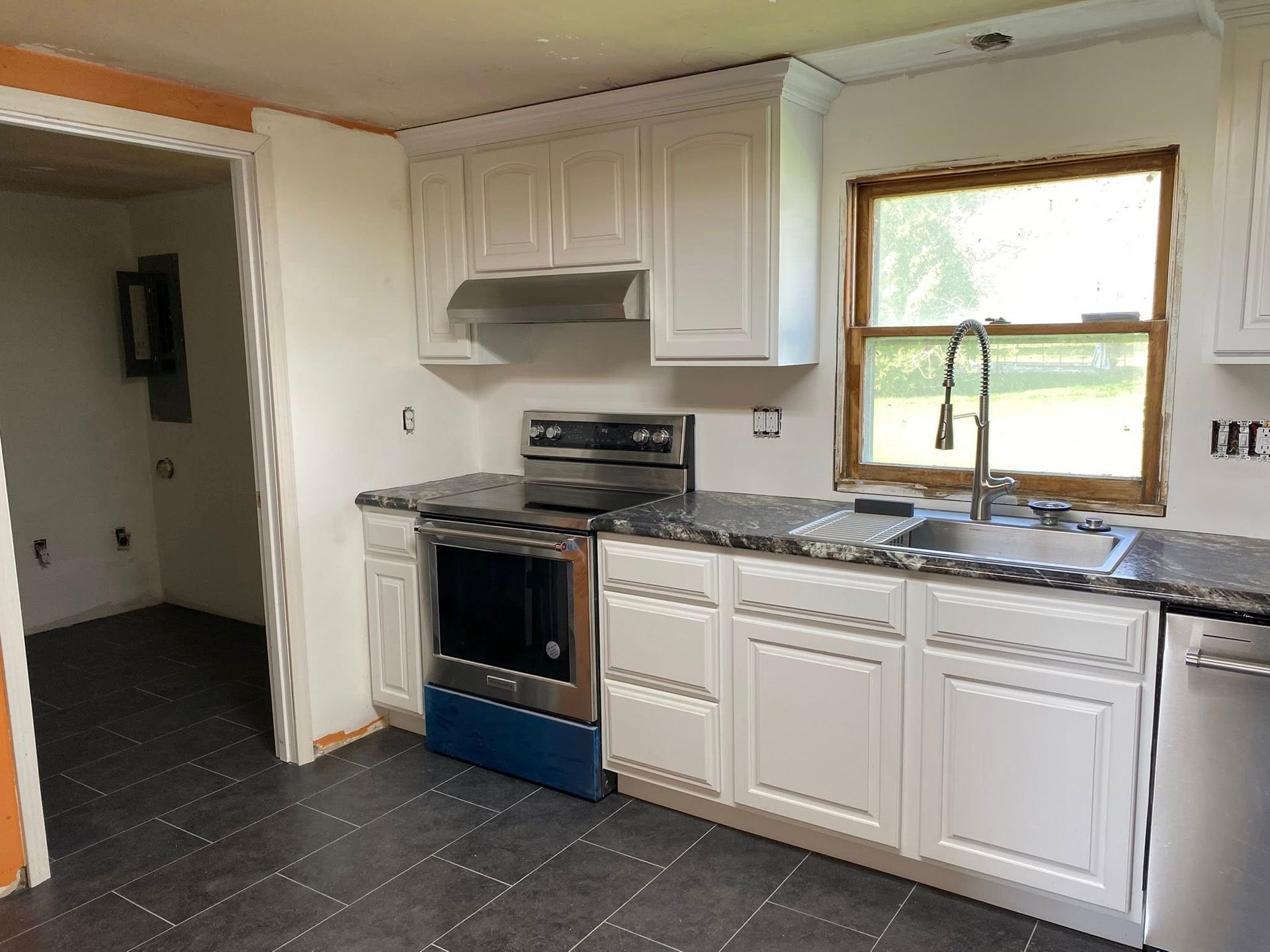 Small kitchen with white cabinets, blue oven, dark tile floor, and a window over the sink