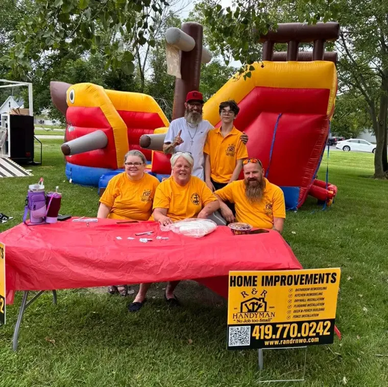 People posing behind a red table at a colorful inflatable event booth outdoors.