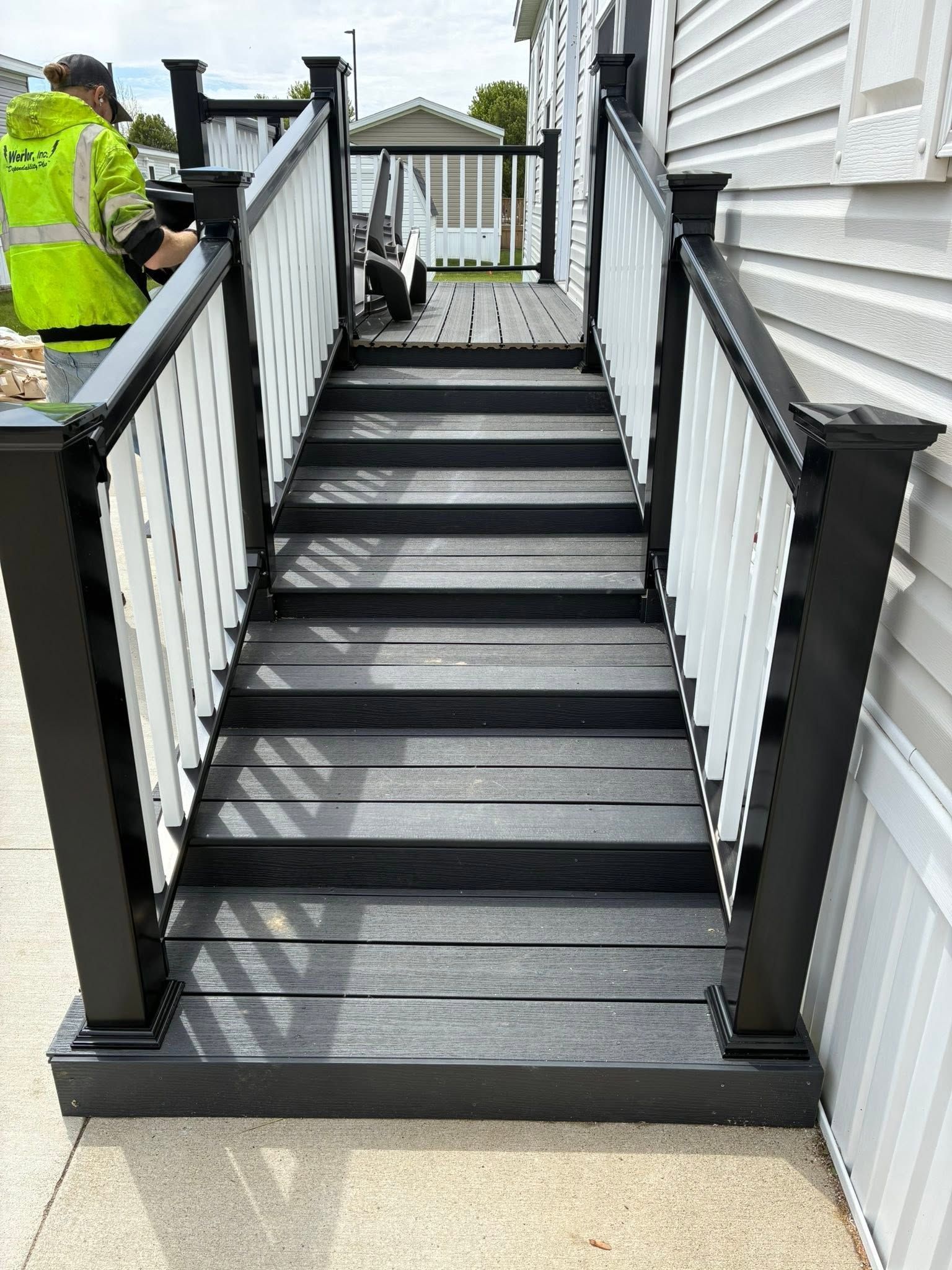 Raised house deck on concrete piers with black railing and stairs over a sloped yard
