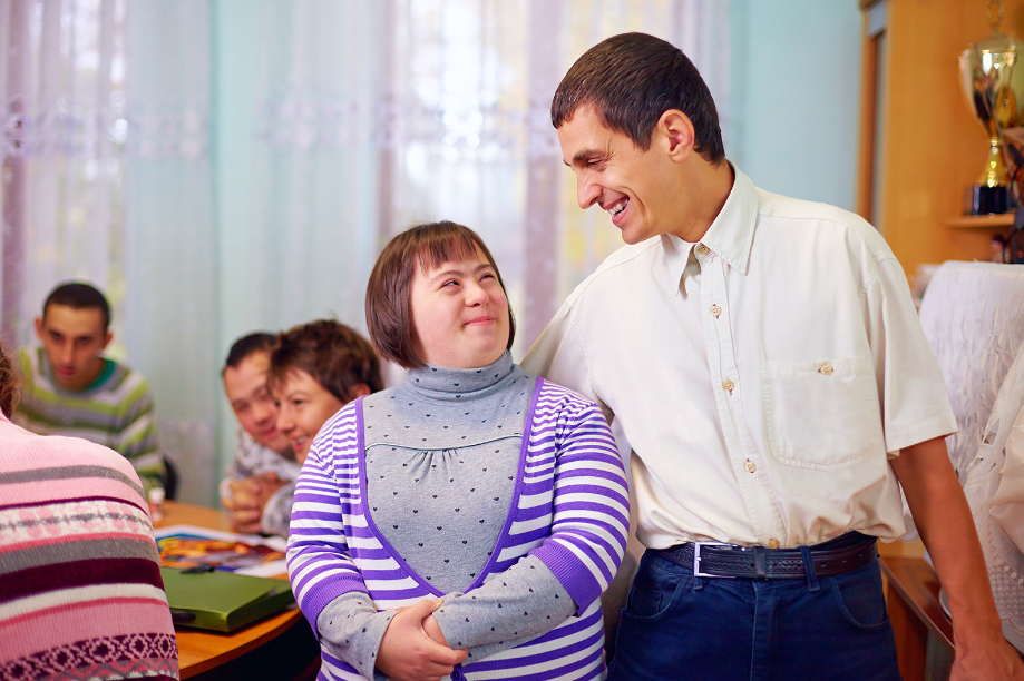 A man and a woman with down syndrome are standing next to each other in a room.