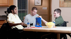 Three men in wheelchairs are playing a game at a table.