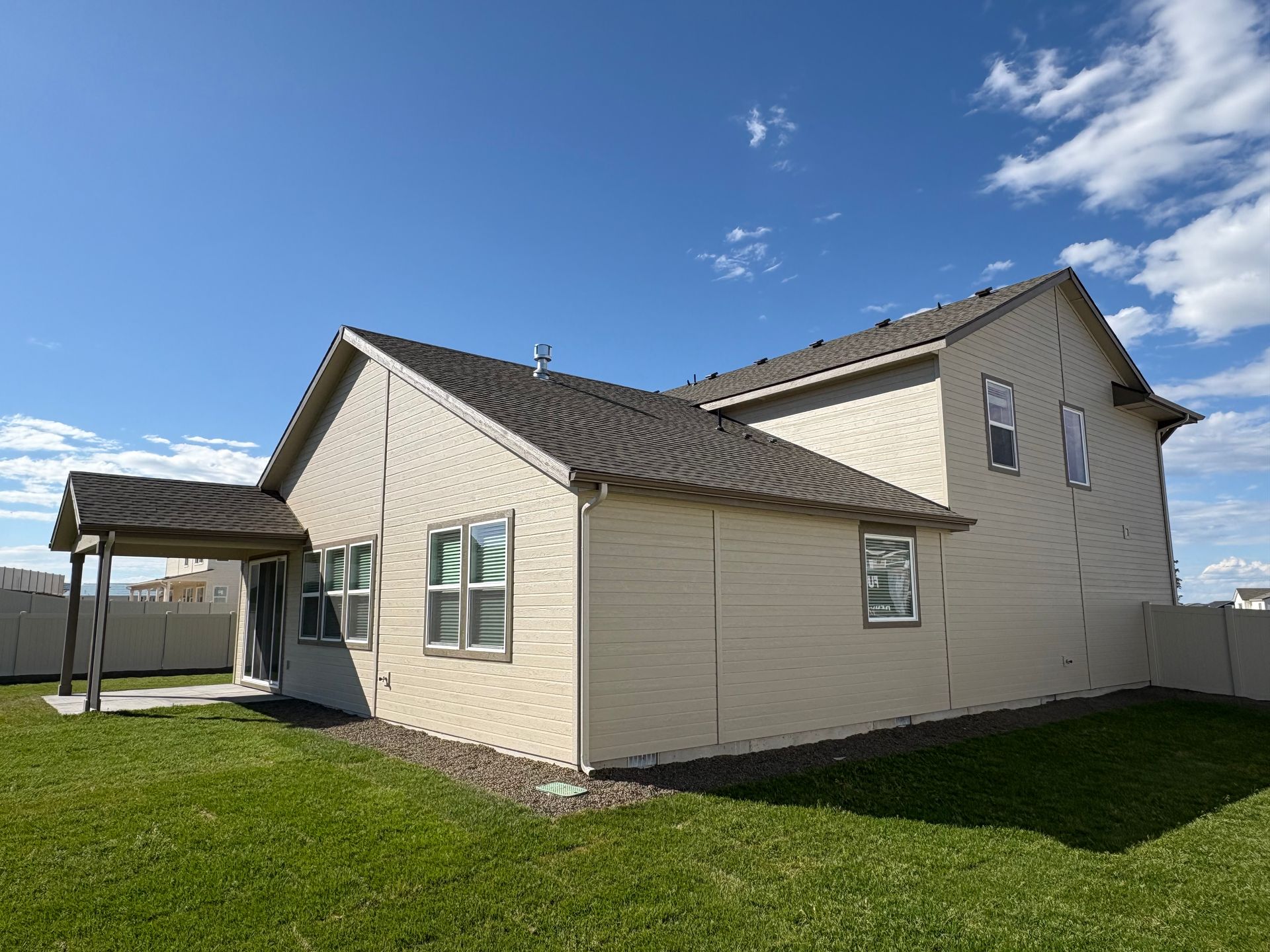 Beige two-story house with a covered patio, set against a blue sky with clouds, on a grassy lawn.
