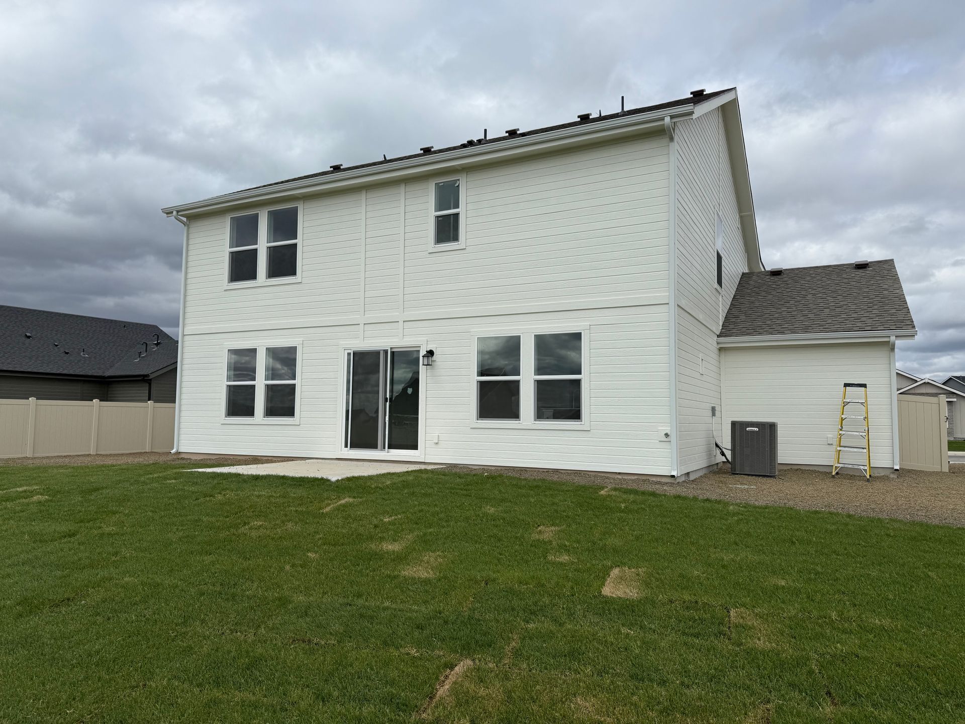Back of a two-story white house with several windows, sliding glass door, and green lawn under a cloudy sky.