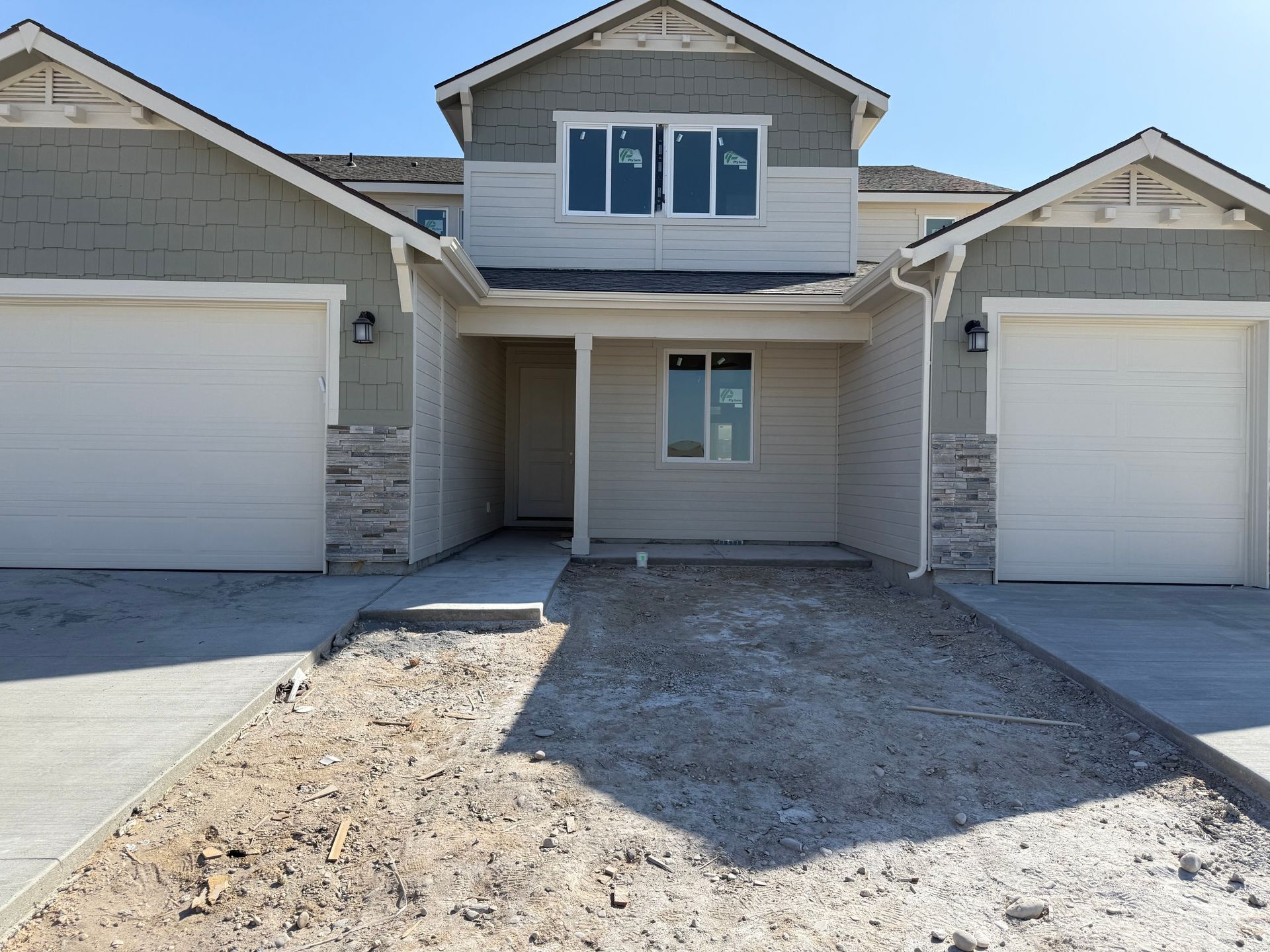 New construction townhomes with light gray siding, stone accents, and unfinished driveway.