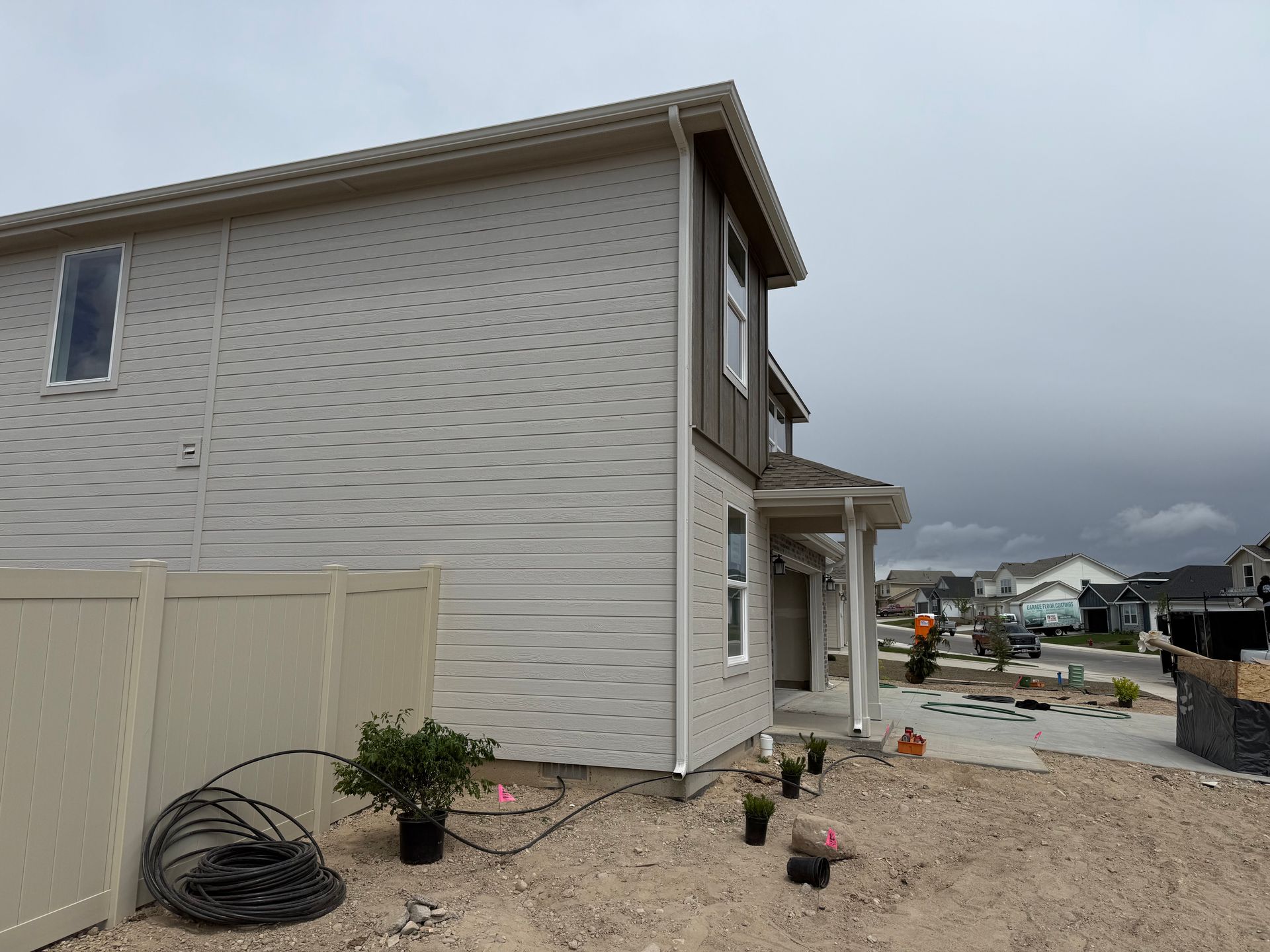 Two-story house with light siding and a small porch. A fence and overcast sky are in the background.