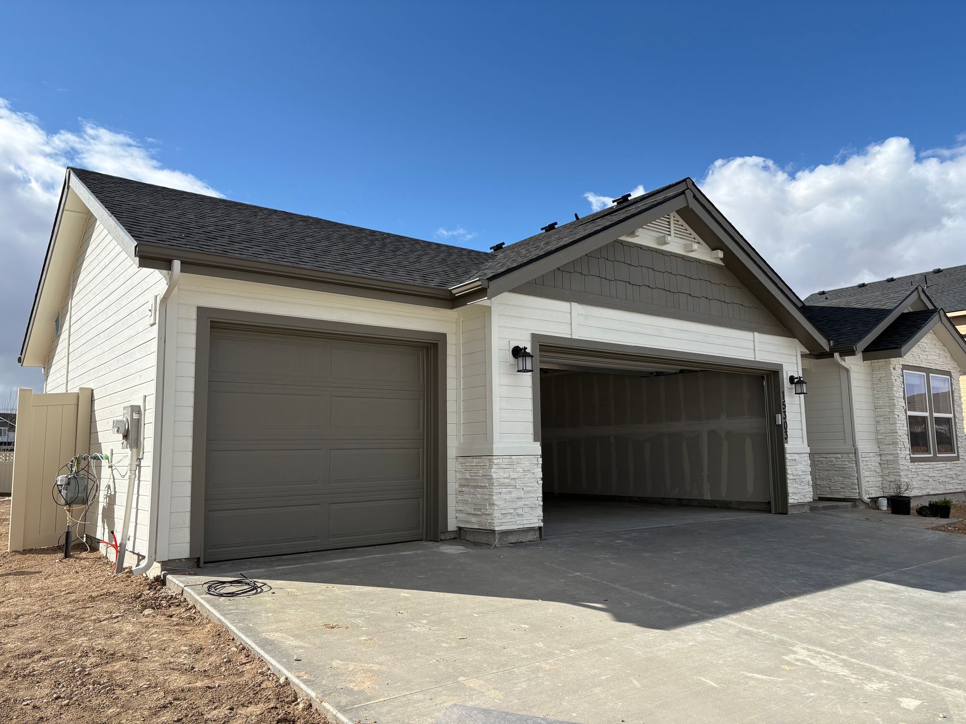 New home with two-car garage, gray doors, white brick exterior, blue sky, and unfinished concrete driveway.