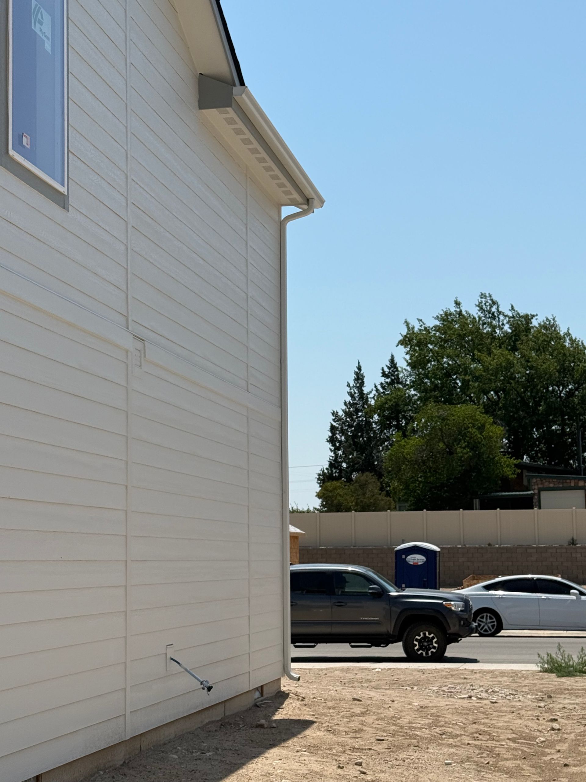 Side view of a white house with a truck and car parked on a street with a blue portable toilet.