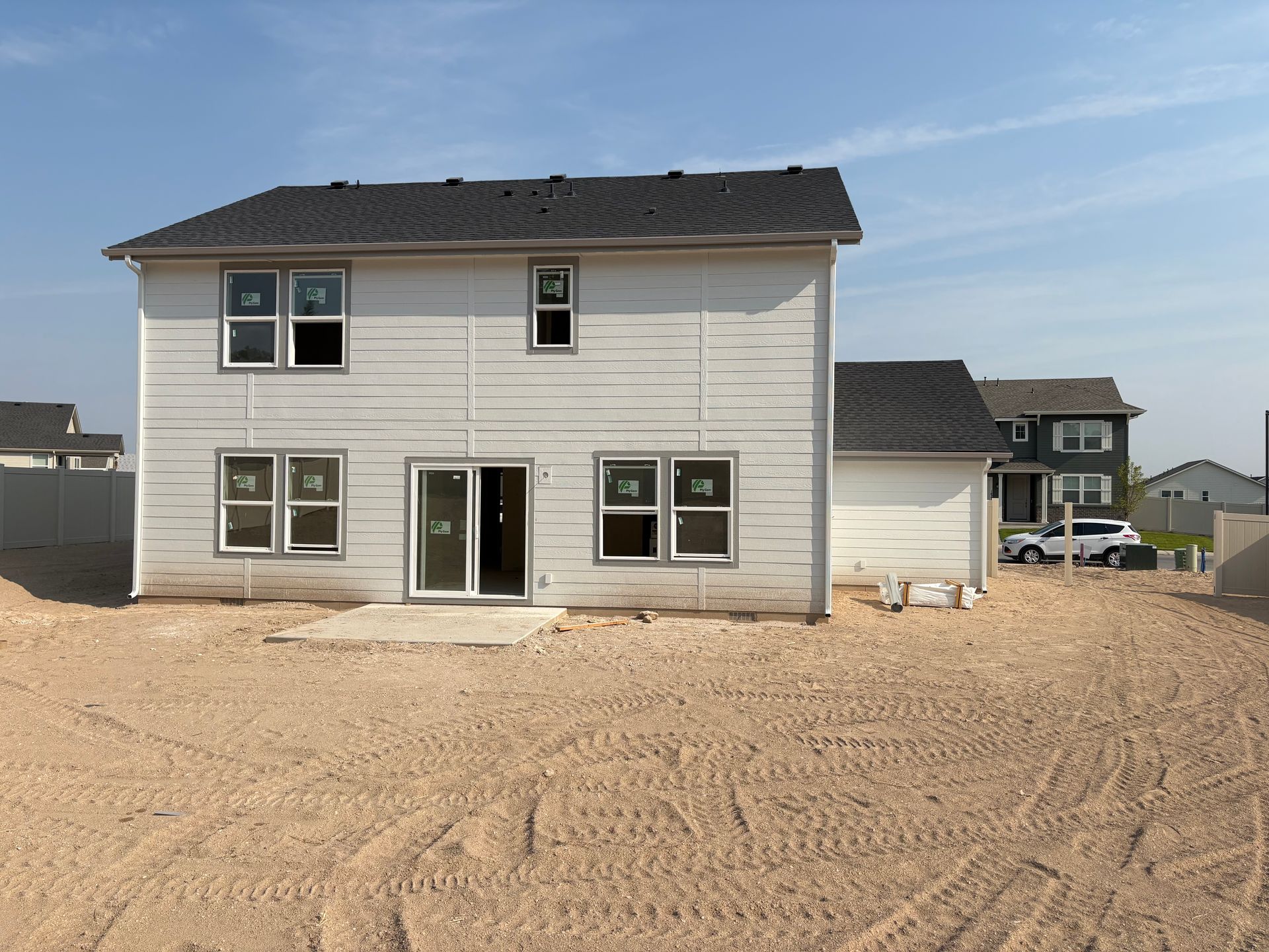 Back of a newly constructed two-story house with white siding and a dark roof, on a dirt lot.