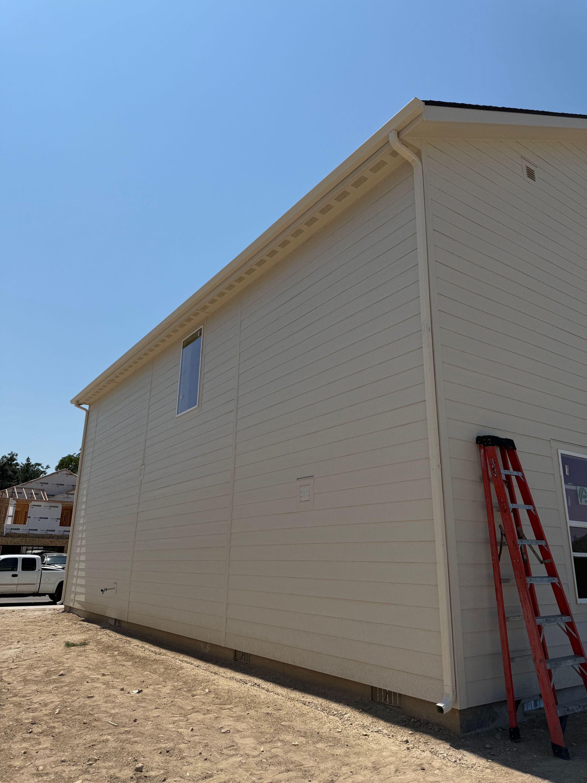 Construction site with beige siding. An orange ladder leans against the wall under a clear blue sky.