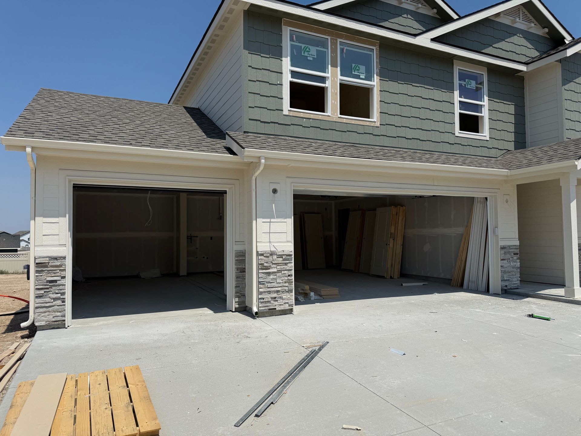 New construction townhome with unfinished garages, gray siding, and a blue sky.