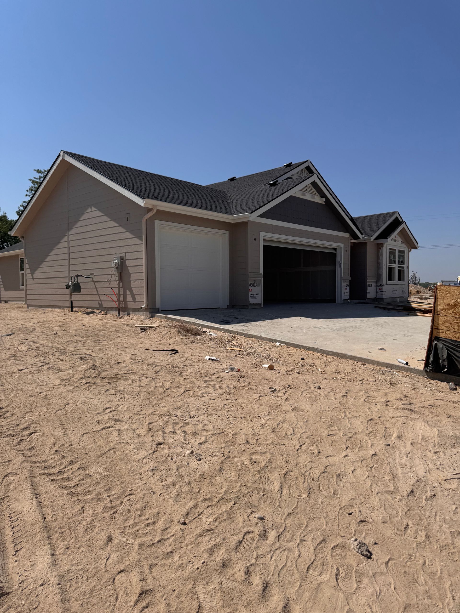 New beige house with a two-car garage under construction, set in dirt, clear sky.