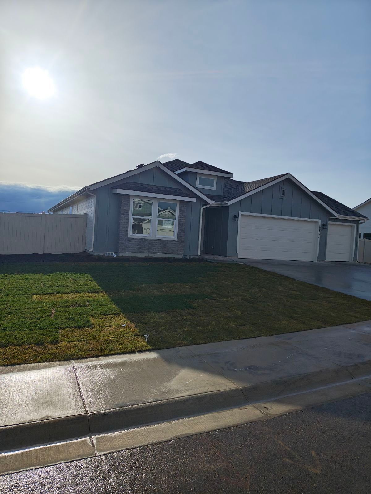 Blue house with a three-car garage, green lawn, and a gray fence on a sunny day.