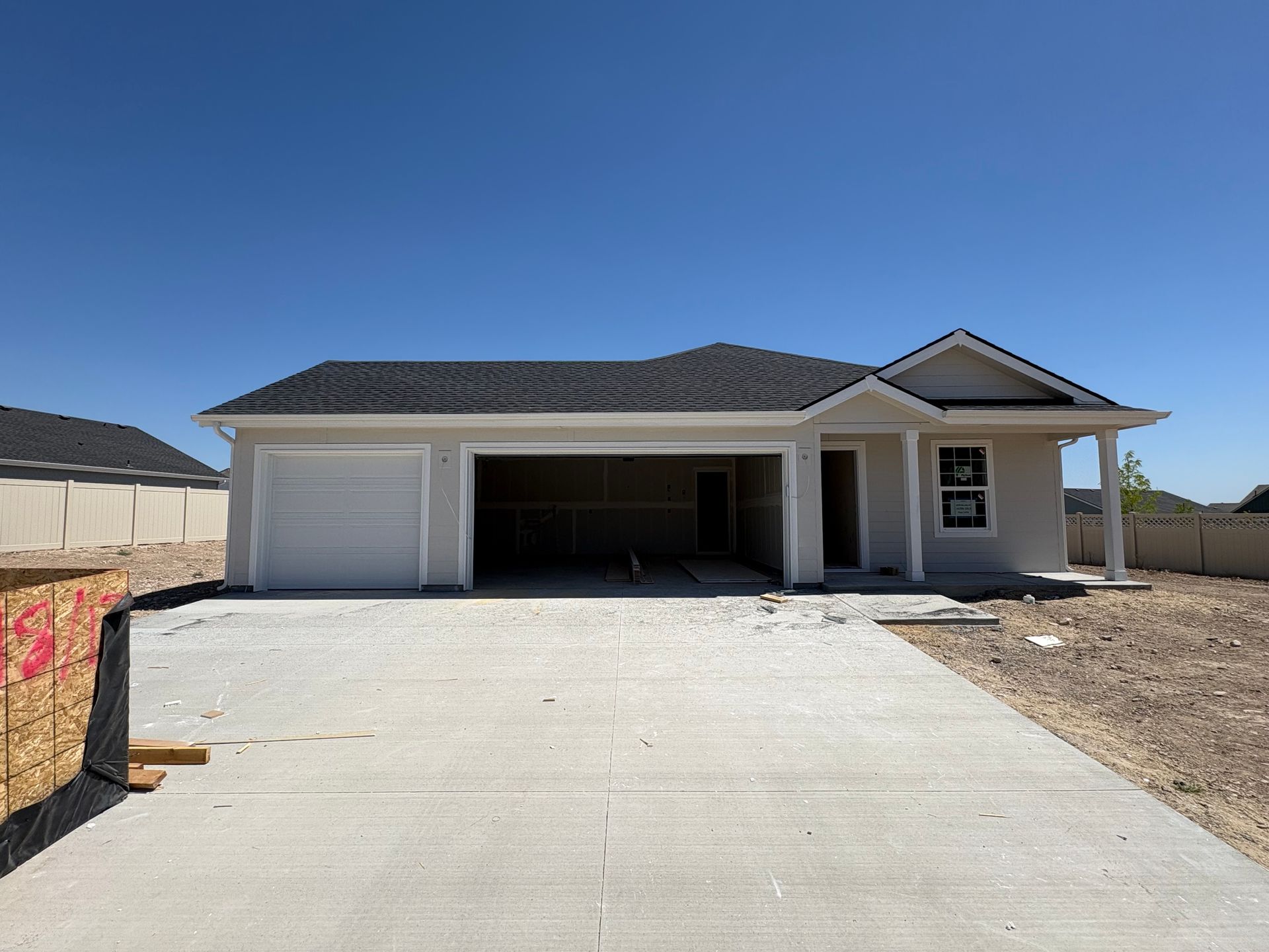 New single-story house under construction with an open garage, concrete driveway, and blue sky.